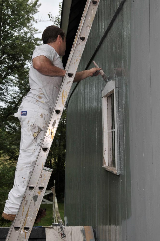 painter on ladder painting window trim