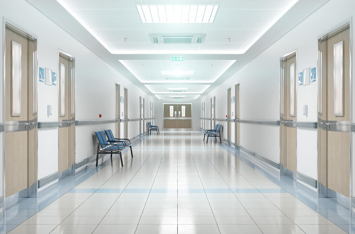 Bright hospital corridor with polished floors and neutral-toned walls. Several blue chairs line the sides, and closed wooden doors are evenly spaced.